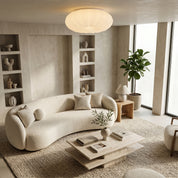 White Bobby flush ceiling light glowing above curved bouclé sofa and travertine coffee table in neutral living room