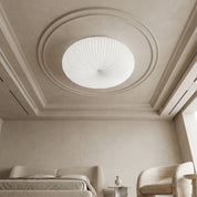 White Bobby flush ceiling light fitted within ornate plaster ceiling medallion above neutral bedroom with bouclé furniture