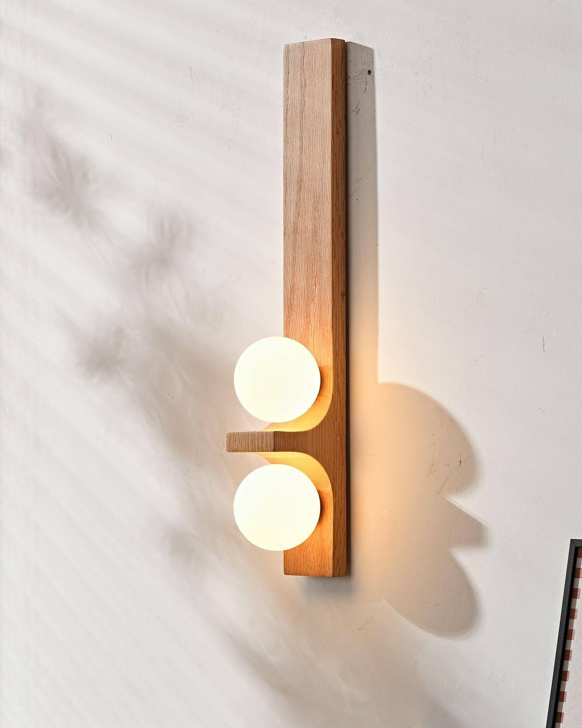 Oak tall Eveline double wall sconce glowing warm white casting soft shadow on white wall