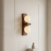 Walnut short Eveline double wall sconce glowing warm white on clean white panelled wall with ceramic vase below