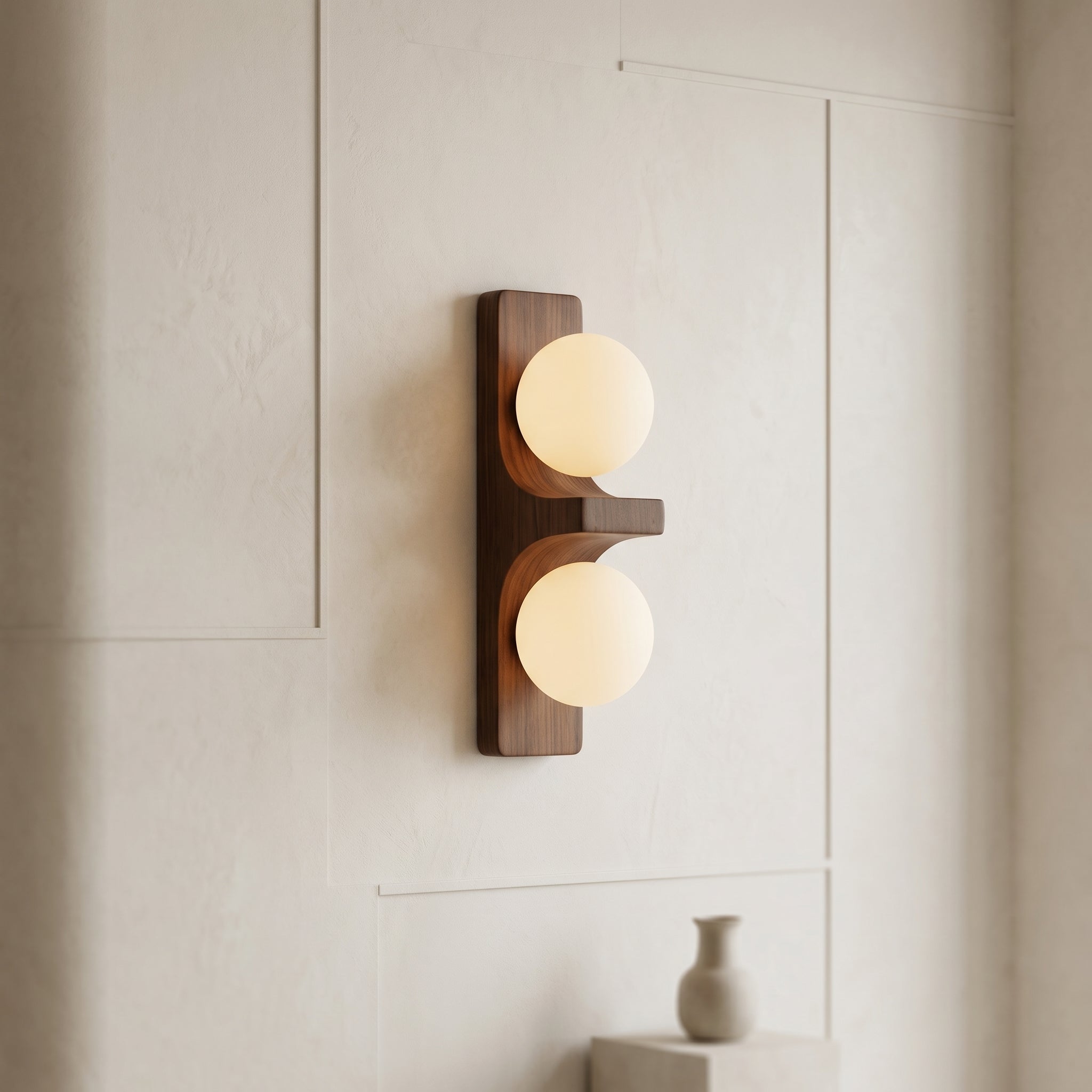 Walnut short Eveline double wall sconce glowing warm white on clean white panelled wall with ceramic vase below