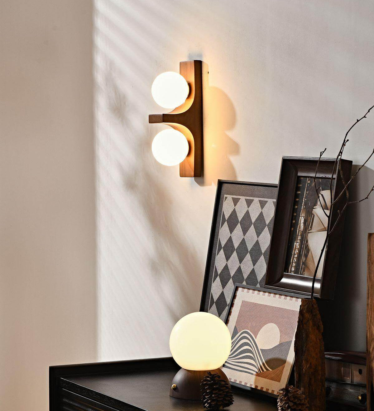 Walnut short Eveline double wall sconce glowing above dark sideboard styled with framed artwork and globe table lamp