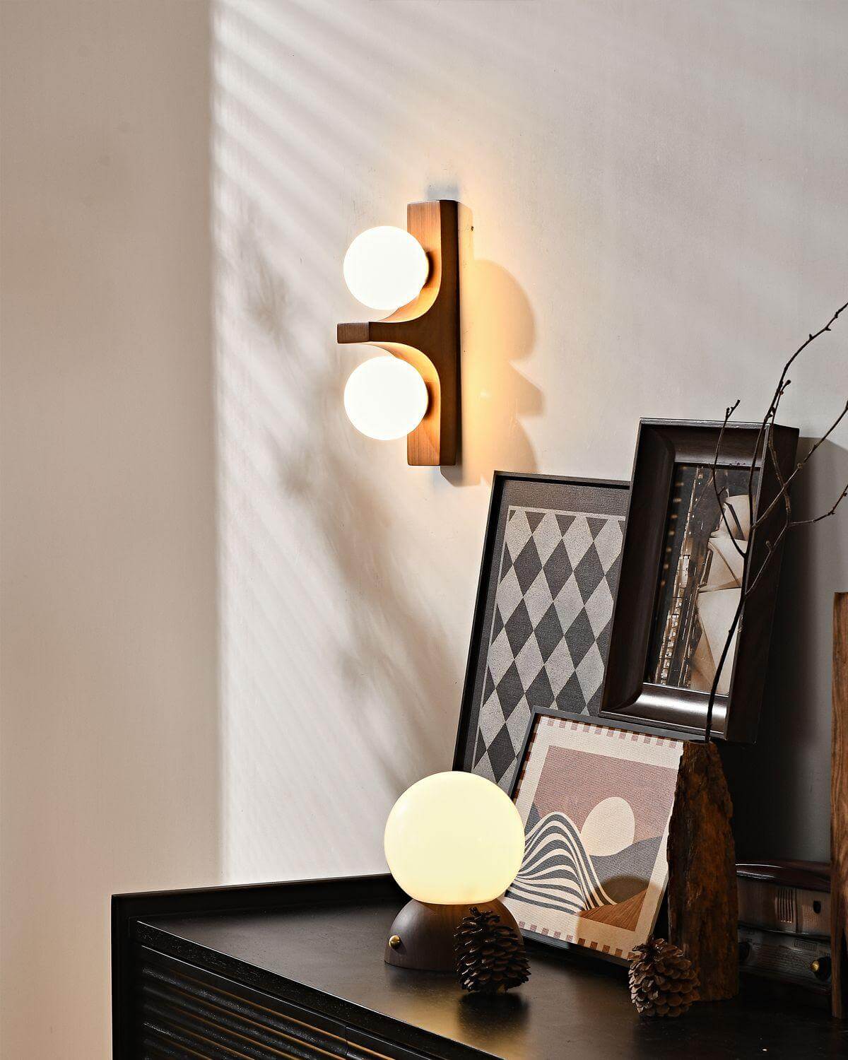 Walnut short Eveline double wall sconce glowing above dark sideboard styled with framed artwork and globe table lamp