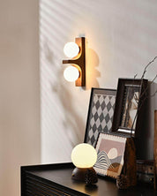 Walnut short Eveline double wall sconce glowing above dark sideboard styled with framed artwork and globe table lamp