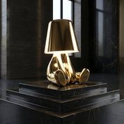 Gold sculptural RayDudes sunset table lamp glowing on black marble pedestal in dark room