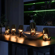 Five gold RayDudes table lamps glowing warm on dark kitchen island at night with green accent lighting