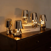 Silver RayDudes table lamps in multiple poses displayed on dark wood dresser with books