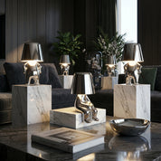 Multiple silver RayDudes table lamps on white marble plinths in dark luxury living room with plants