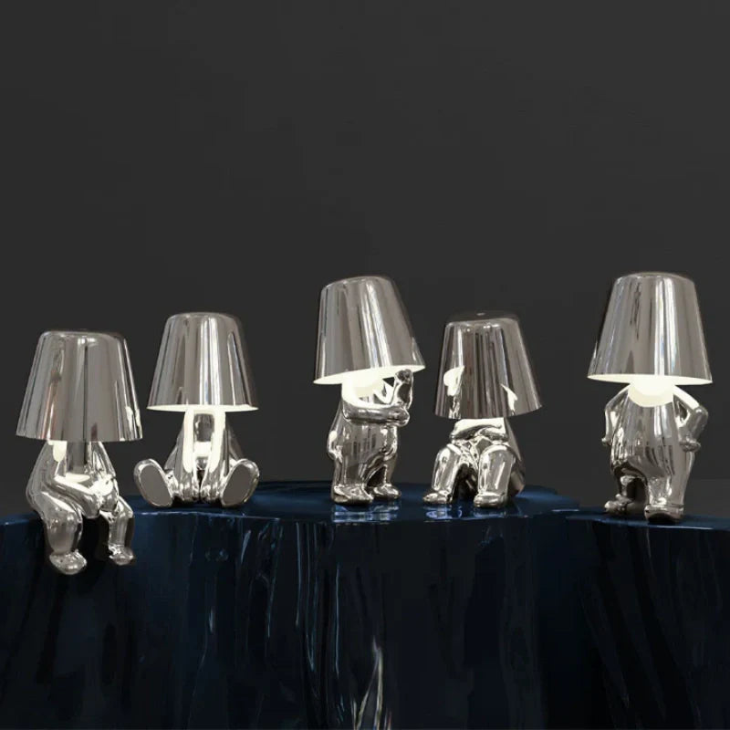 Five silver RayDudes sculptural table lamps in different poses displayed on dark blue reflective table