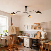 Black 3-arm Serge Mouille ceiling light mounted above art studio with easels canvases and sculptor bust