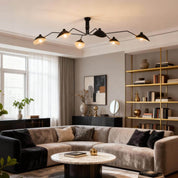 Black 6-arm Serge Mouille ceiling light above grey velvet sectional sofa in living room with gold shelving