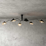 Black 6-arm Serge Mouille inspired ceiling light with brass joints spanning wide on concrete ceiling product shot