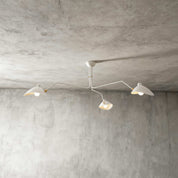 White 3-arm Serge Mouille inspired ceiling light with brass joints on concrete ceiling product shot