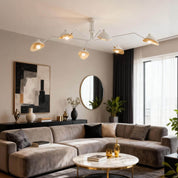 White 6-arm Serge Mouille ceiling light above grey velvet sofa in living room with gold accents and round mirror