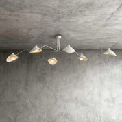 White 6-arm Serge Mouille inspired ceiling light with brass joints spanning wide on concrete ceiling product shot